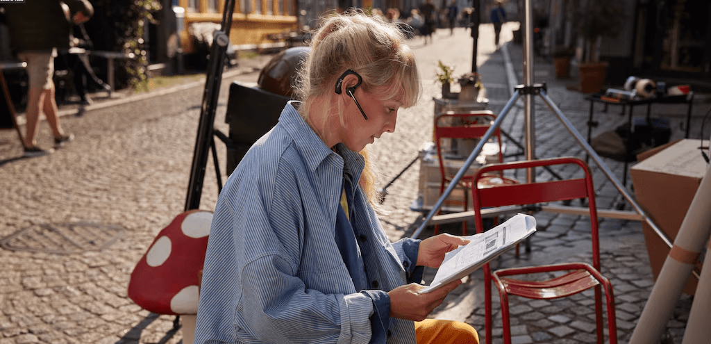 Profesional usando auriculares Bluetooth mientras lee documentos en un caf&eacute; al aire libre